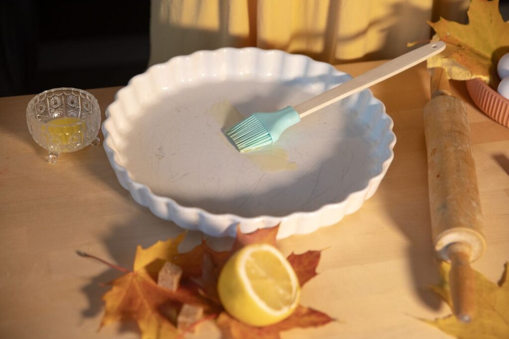 Bakform med pensel, citron, höstlöv och köksredskap på träbord
