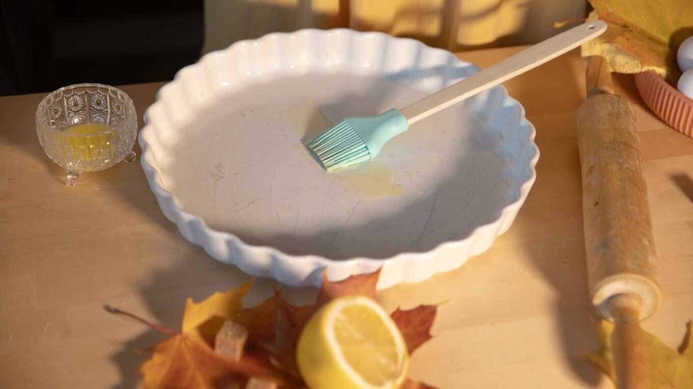 Bakform med pensel, citron, höstlöv och köksredskap på träbord